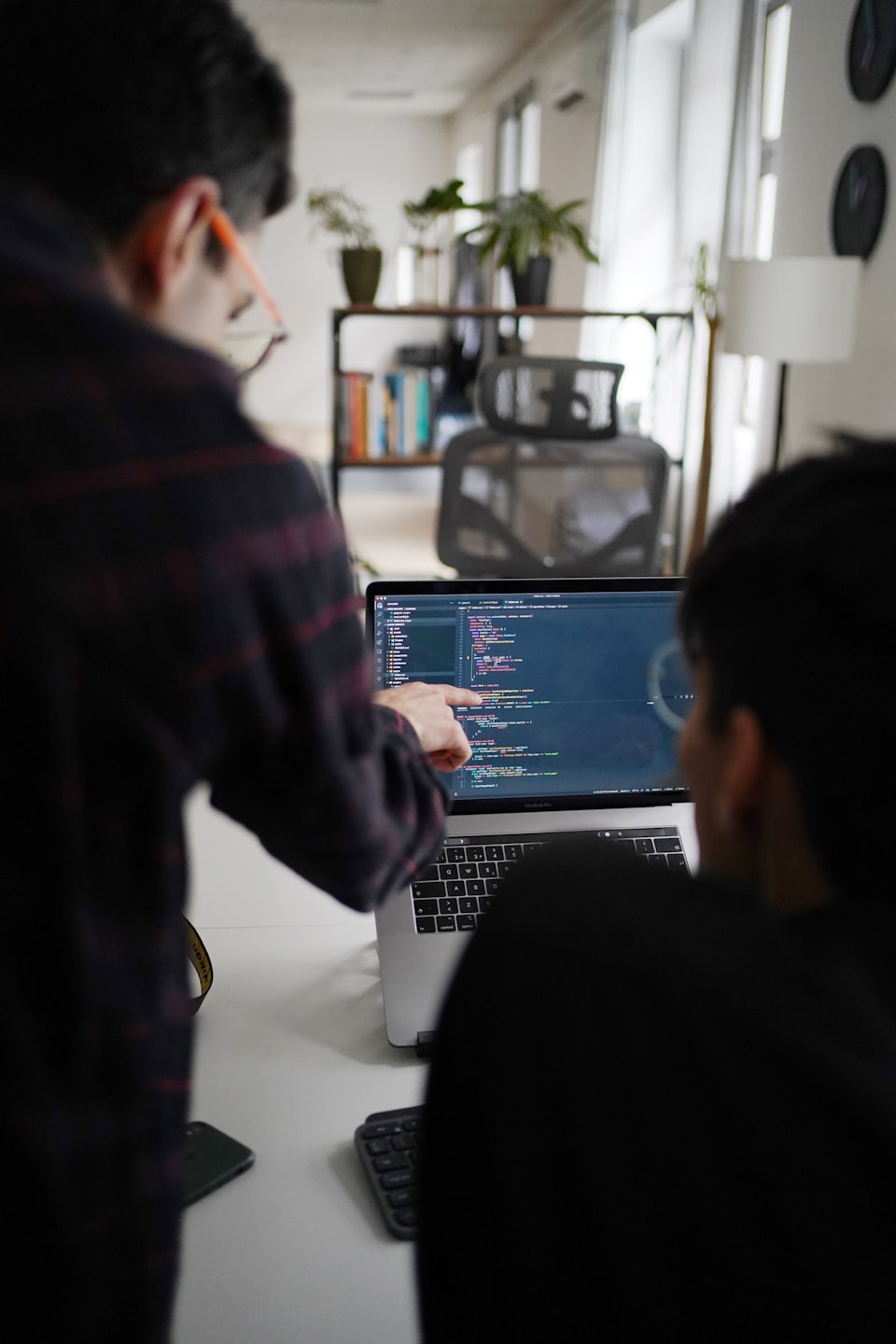 Two colleagues collaborate over code on a laptop.