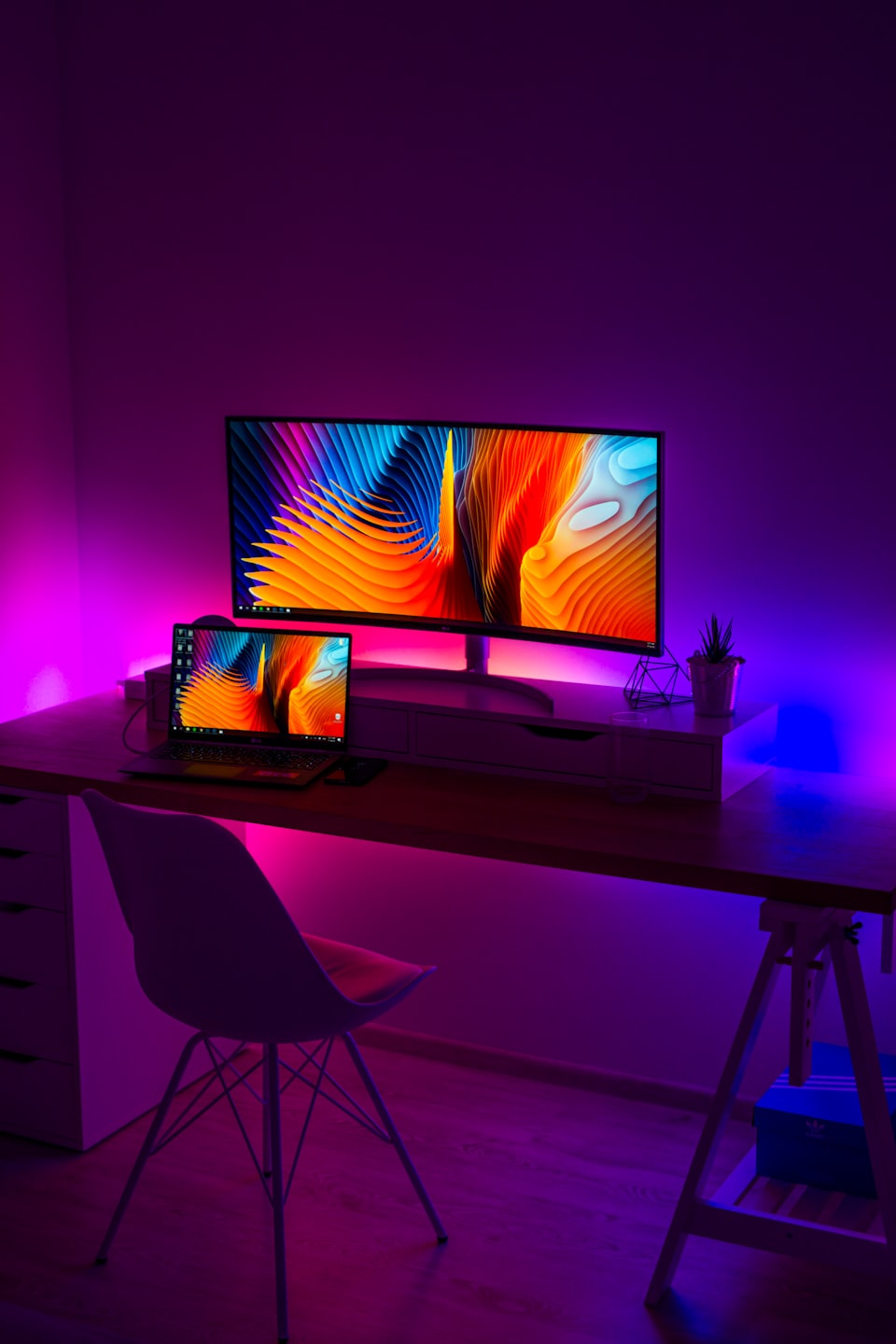 Modern home office with curved monitor and laptop displaying colorful wallpapers.